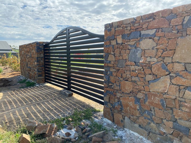Black horizontal-slat sliding entrance gate on a stone-pillar driveway